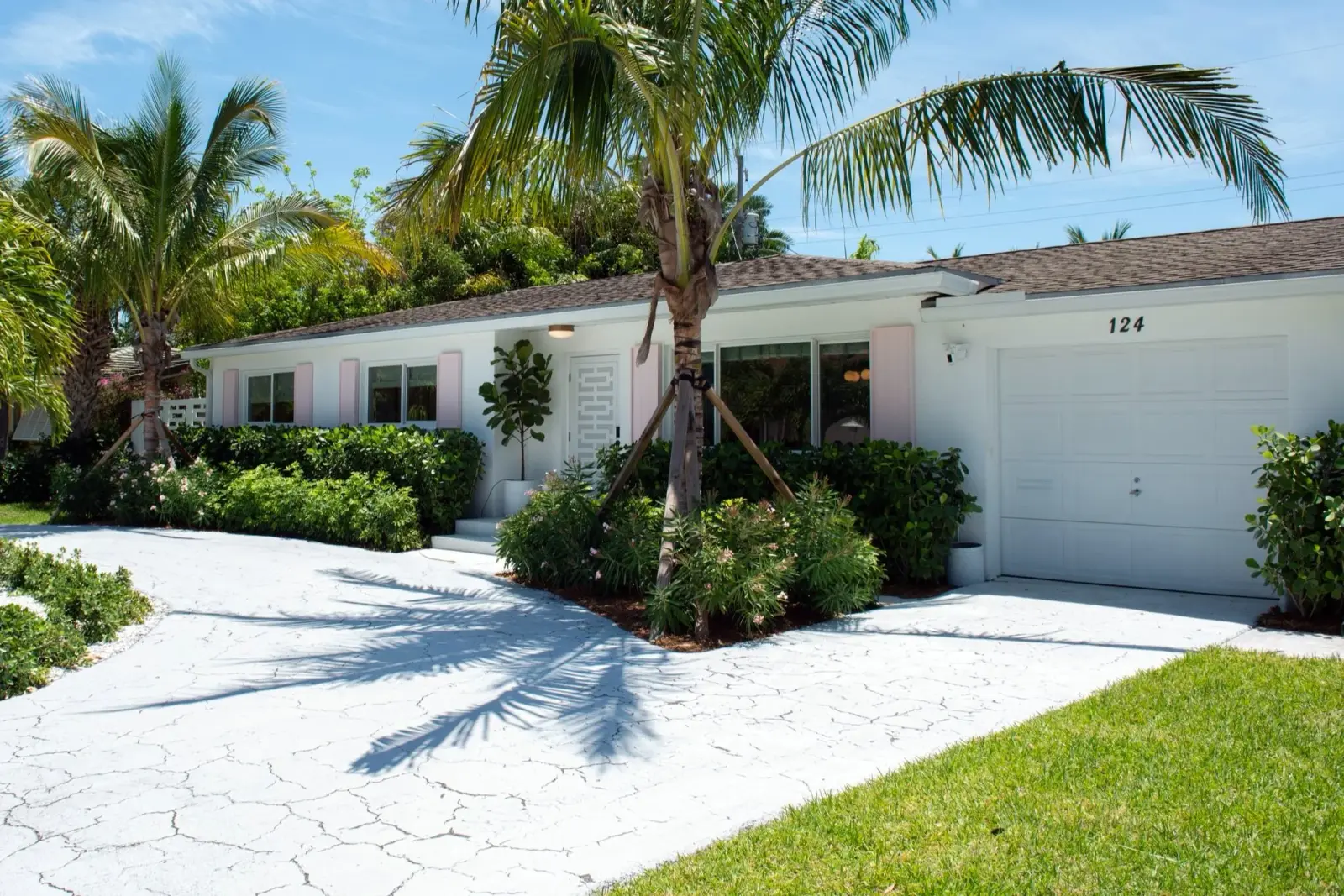 White mid-century bungalow with pink shutters under mature palms