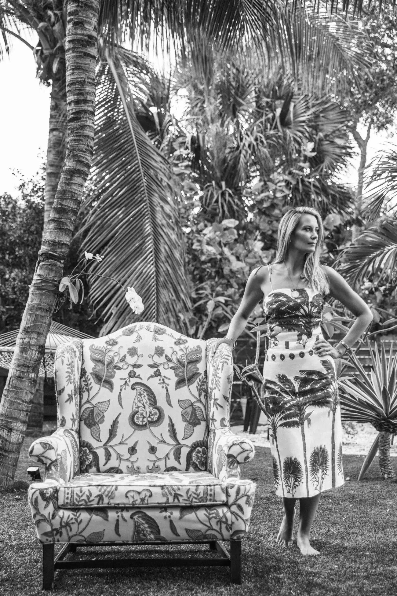 Libby Lary standing beside a crewel-work wingchair beneath the palms