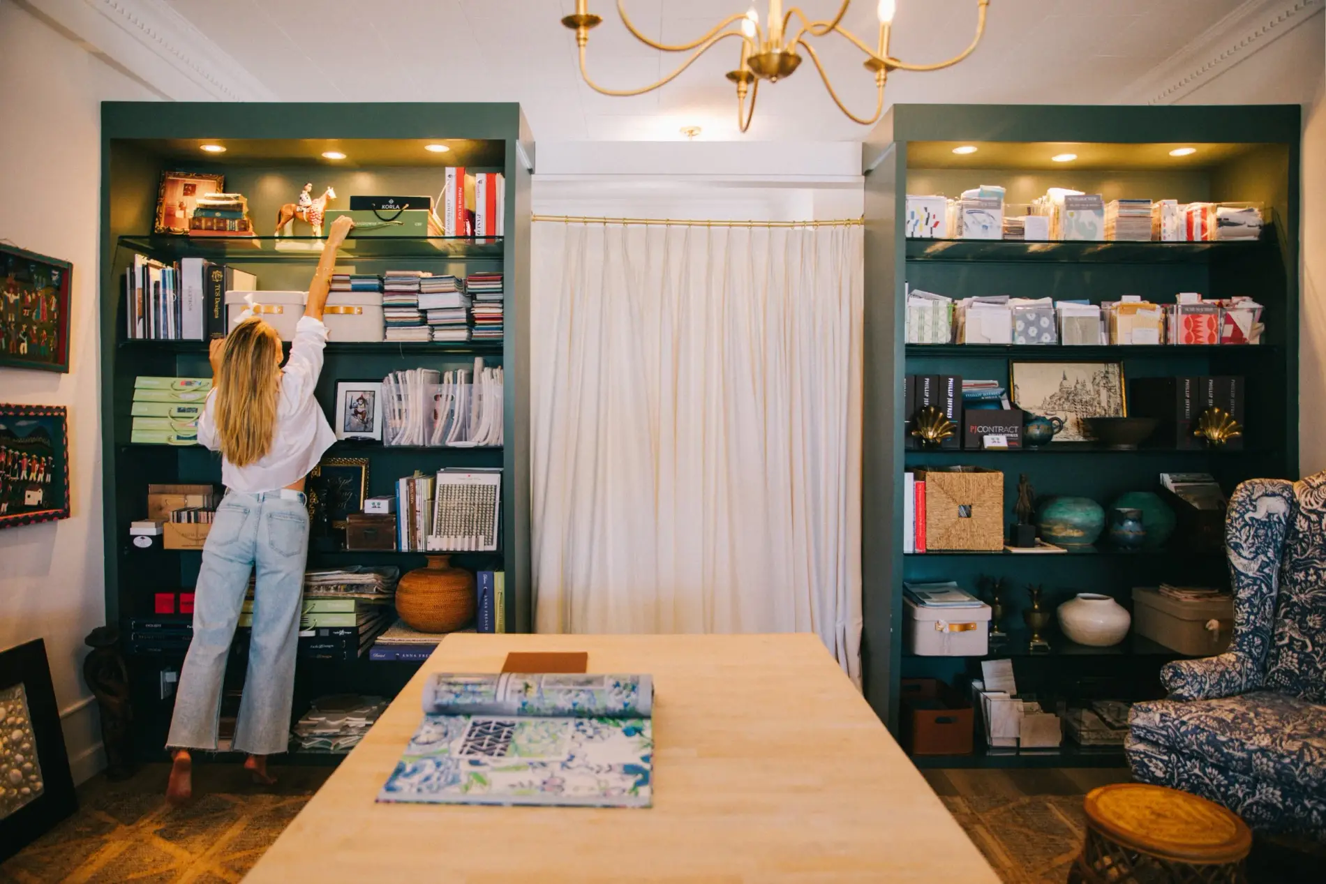 The Elizabeth Gray Homes studio: green shelving stacked with fabric samples beneath a brass chandelier